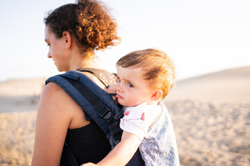 Back of a woman carrying a baby in a baby carrier outdoors during sunset