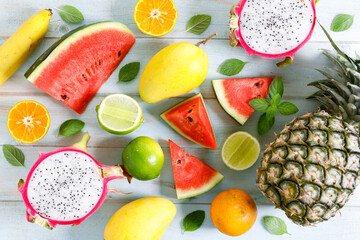 variety of summer fruits, watermelon pineapple mango lime orange dragonfruit, flat lay on light blue wooden background.