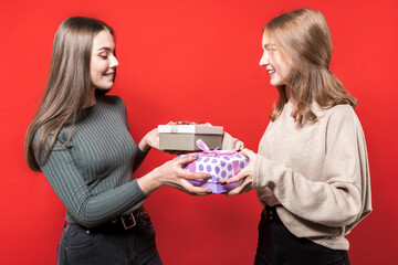 Two cute beautiful girlfriends give each other gifts. Adorable girls exchange gift boxes. Friends. New year gifts. Christmas. Birthday. Sisters.