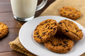 A bunch of delicious chocolate chip cookies on a white plate with a cup of milk. Close Up.