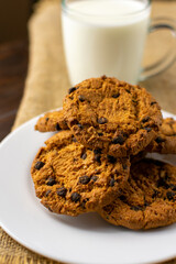 A bunch of delicious chocolate chip cookies on a white plate with a cup of milk. Close Up.