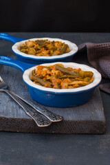 Vegetable stew with green beans and cauliflower and sweet peppers in a ceramic bowl on a wooden stand.
