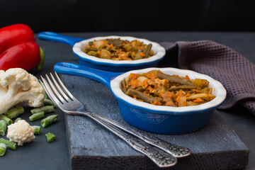 Vegetable stew with green beans and cauliflower and sweet peppers in a ceramic bowl on a wooden stand.
