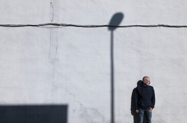 Adult man standing against white wall with shadow of street lamp