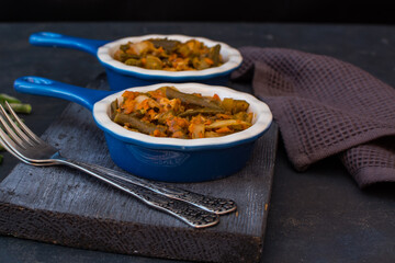 Vegetable stew with green beans and cauliflower and sweet peppers in a ceramic bowl on a wooden stand.

