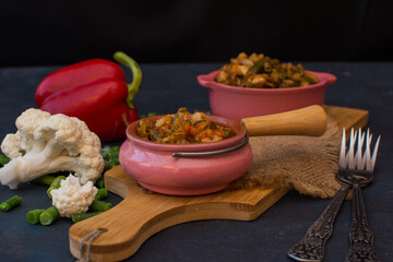 Vegetable stew with green beans and cauliflower and sweet peppers in a ceramic bowl on a wooden stand.
