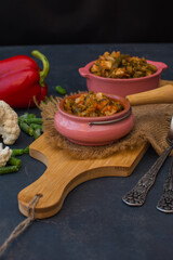 Vegetable stew with green beans and cauliflower and sweet peppers in a ceramic bowl on a wooden stand.

