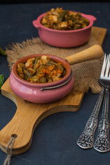 Vegetable stew with green beans and cauliflower and sweet peppers in a ceramic bowl on a wooden stand.
