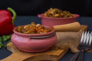 Vegetable stew with green beans and cauliflower and sweet peppers in a ceramic bowl on a wooden stand.
