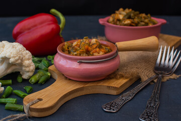 Vegetable stew with green beans and cauliflower and sweet peppers in a ceramic bowl on a wooden stand.

