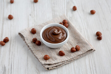 Homemade Chocolate Hazelnut Spread in a Bowl on a white wooden background, side view.