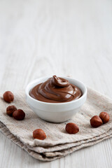 Homemade Chocolate Hazelnut Spread in a Bowl on a white wooden background, side view. Copy space.