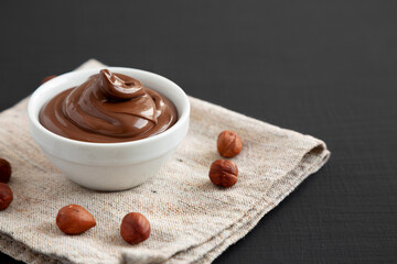 Homemade Chocolate Hazelnut Spread in a Bowl on a black background, side view. Space for text.