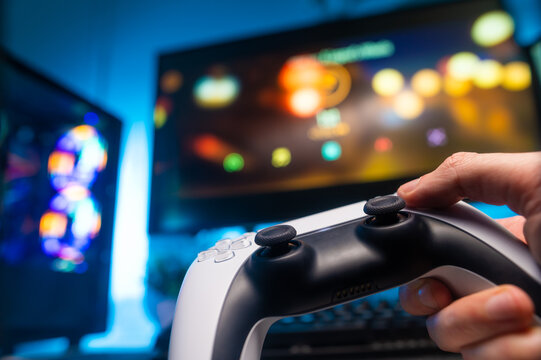 The gamer holds a gamepad in his hand. Close-up. Large personal computer monitor. Neon lighting. Technological background. Video games, prizes, winnings, computer equipment.