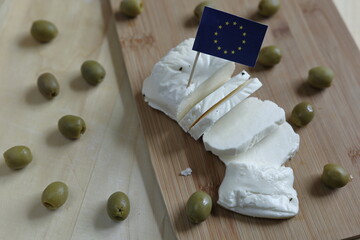 Traditional Cypriot cheese called halloumi decorated with EU flag and olives, on cut board top view, listed as registered local original product