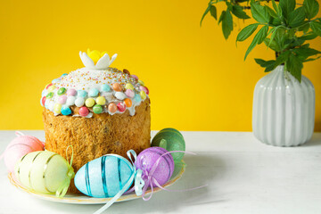 Easter cake with painted eggs on a platter in a white table. Traditional festive food. Yellow background