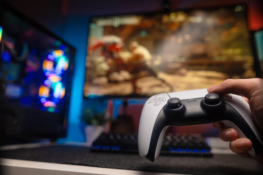 A gamer plays a video game on a large TV screen. He has a trendy modern gamepad in his hand. Fun time with friends. Prizes, win.Evening. The room is lit with blue neon light. - Powered by Adobe