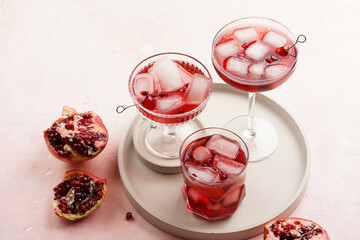 three glasses with fresh pomegranate juice with one real pomegranate on concrete tray on pink background