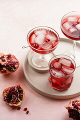 three glasses with fresh pomegranate juice with one real pomegranate on concrete tray on pink background