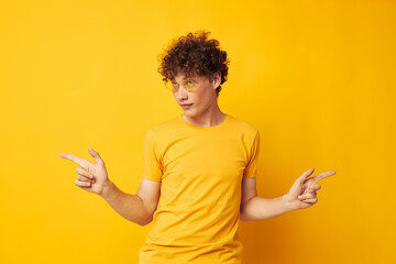 Young curly-haired man wearing stylish glasses yellow t-shirt posing isolated background unaltered