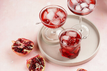 three glasses with fresh pomegranate juice with one real pomegranate on concrete tray on pink background
