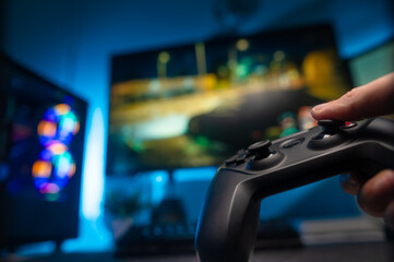 Video games. A modern gamepad in the player's hand. Large screen TV. Online games with friends, youth culture, modern technologies, virtual reality. Blue neon lighting.