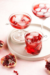 three glasses with fresh pomegranate juice with one real pomegranate on concrete tray on pink background