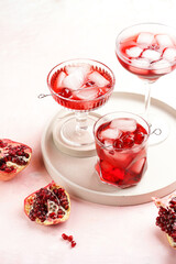 three glasses with fresh pomegranate juice with one real pomegranate on concrete tray on pink background