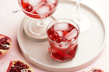 three glasses with fresh pomegranate juice with one real pomegranate on concrete tray on pink background