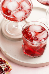 three glasses with fresh pomegranate juice with one real pomegranate on concrete tray on pink background