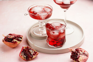 three glasses with fresh pomegranate juice with one real pomegranate on concrete tray on pink background
