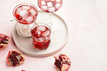 three glasses with fresh pomegranate juice with one real pomegranate on concrete tray on pink background