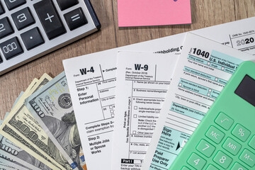 tax forms 1040 are blank to fill out and dollars are sloppily scattered on a wooden table.