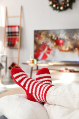 Woman in cute knitted socks watching TV at home, closeup