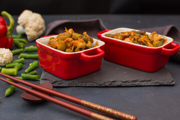 Vegetable stew with green beans and cauliflower in a red ceramic bowl.