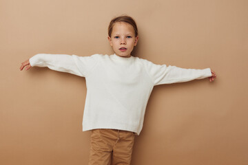 Portrait of happy smiling child girl in white sweater posing hand gestures beige background