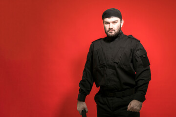 Fototapeta na wymiar A male security guard in a black uniform and a cap on a red background. Bodyguard. Private security. Defender. Mercenary.