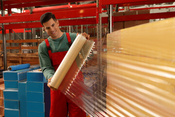 Worker wrapping boxes in stretch film at warehouse - obrazy, fototapety, plakaty