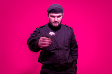 A male guard in black uniform and a cap holds a flower forward. The bodyguard gives a succulent. Defender of the law and order. Military. Mercenary. Handsome brutal man.