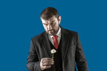 Sexy male look. International women's day. Women's holiday. Brutal person. A man in a business suit with a red tie holds a daisy flower in his hands. Romantic