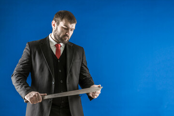 A bearded man in a suit with a red tie with a long knife in his hands. The killer examines his...