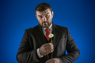 Romantic. A man in a business suit with a red tie holds a daisy flower in his hands. Brutal person. Women's holiday. International women's day. Sexy male look