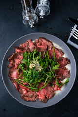 Marbled beef carpaccio with arugula and parmesan cheese. Black background