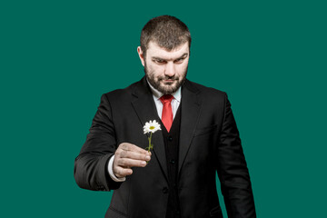 Brutal person. International women's day. Romantic. Sexy male look. Women's holiday. A man in a business suit with a red tie holds a daisy flower in his hands