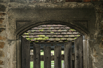 Torbogen aus Stein mit Holzlattentüre vor moosbedecktem Dach an Klostergarten