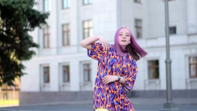 A caucasian teenage girl with pink hair is dancing hip hop on a city street on a summer day.Generation Z.Slow motion.