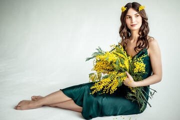 A beautiful young woman with a bouquet of mimosa flowers on a white background in a green dress...