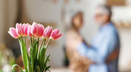 Beautiful bouquet of fresh pink tulips against dancing senior couple in love on blurred background