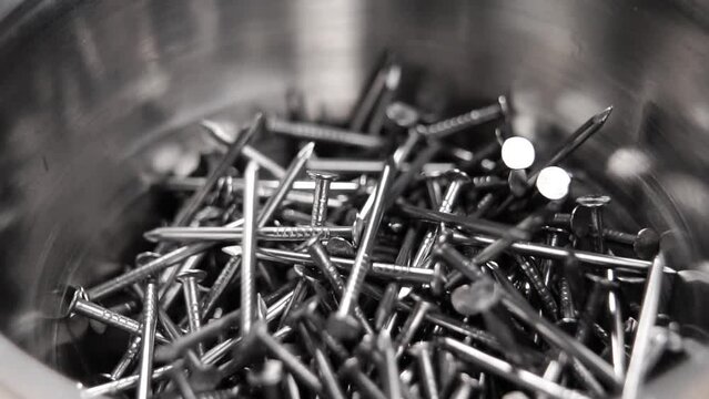 Metallic carpenter nails falling in steel container. Slow motion. Macro shot