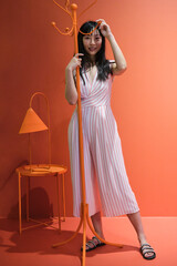 Young asian woman pose with a red orange monochrome coat rack. Studio shot.
